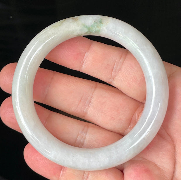 Hand holding a 57.8mm natural Grade A Burmese jadeite bangle in icy milky white with imperial and apple green veins, item JB155