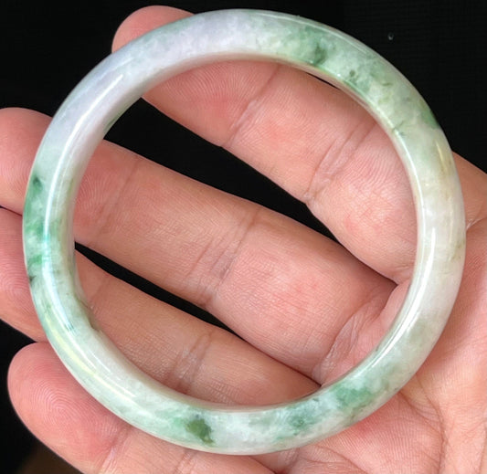 Hand holding a 58.5mm natural Grade A Burmese jadeite bangle in icy milky white and greyish lavender with imperial green, item JB505