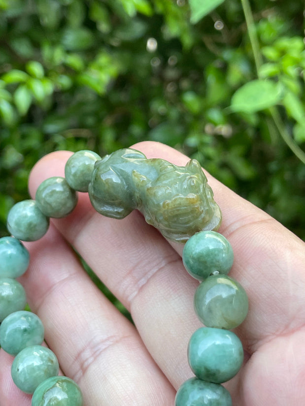 Handcrafted genuine Grade A Burmese jadeite stretch bracelet showcasing beautiful mossy green beads with a hand-carved Pixiu pendant and official certification
