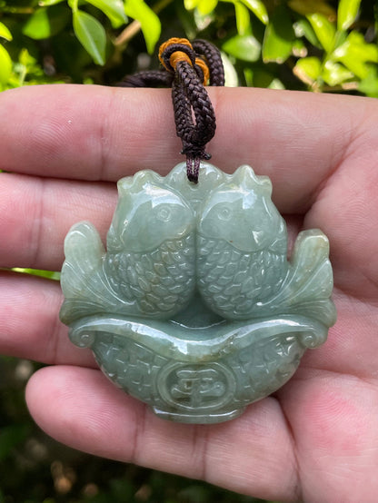 Close-up of a natural Grade A certified Burmese jadeite pendant featuring bluish moss green hues and brown inclusions hand-carved with a twin fish motif, item JP037